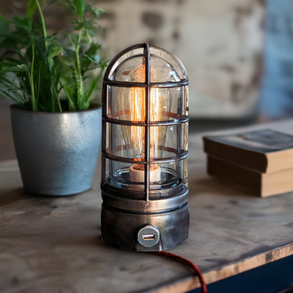 A vintage-style metal cage lamp with a warm glowing light bulb inside, sitting on a wooden surface