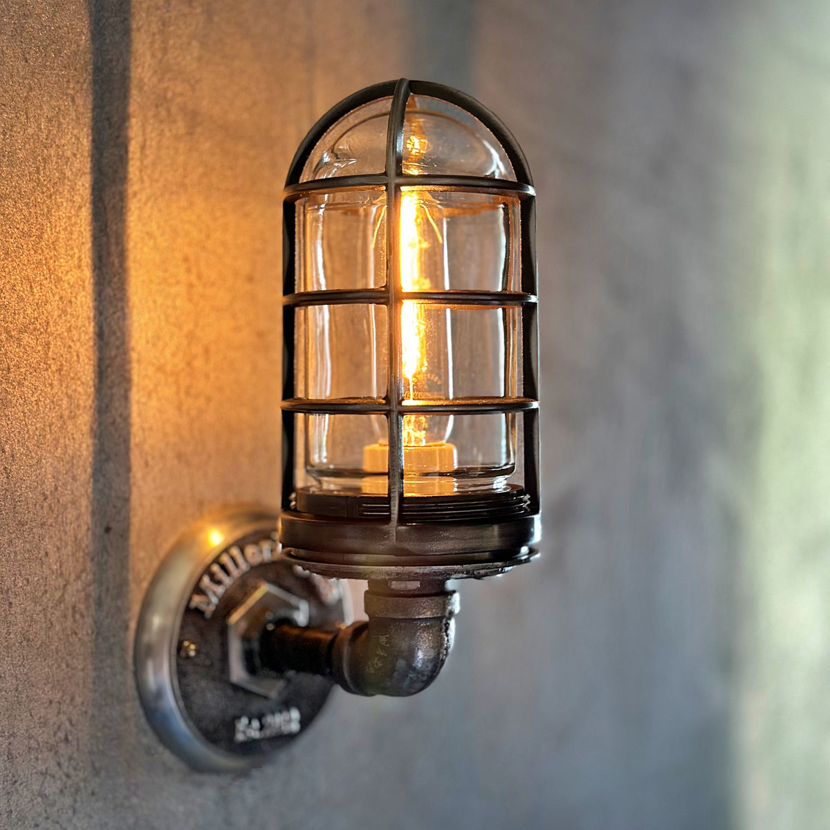 An old-fashioned metal wall sconce with a caged light bulb, mounted on a textured concrete or plaster wall