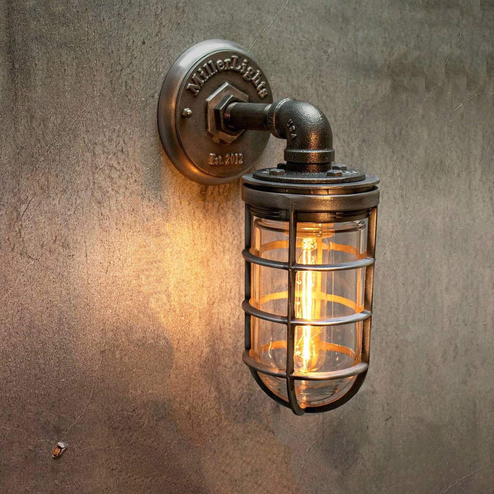 a vintage Industrial-style wall sconce with a metal cage and glowing light bulb against a concrete wall 