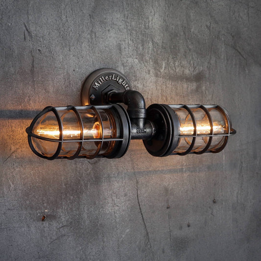 A vintage-style industrial wall light fixture with two metal cages surrounding the bulbs mounted on a concrete wall 